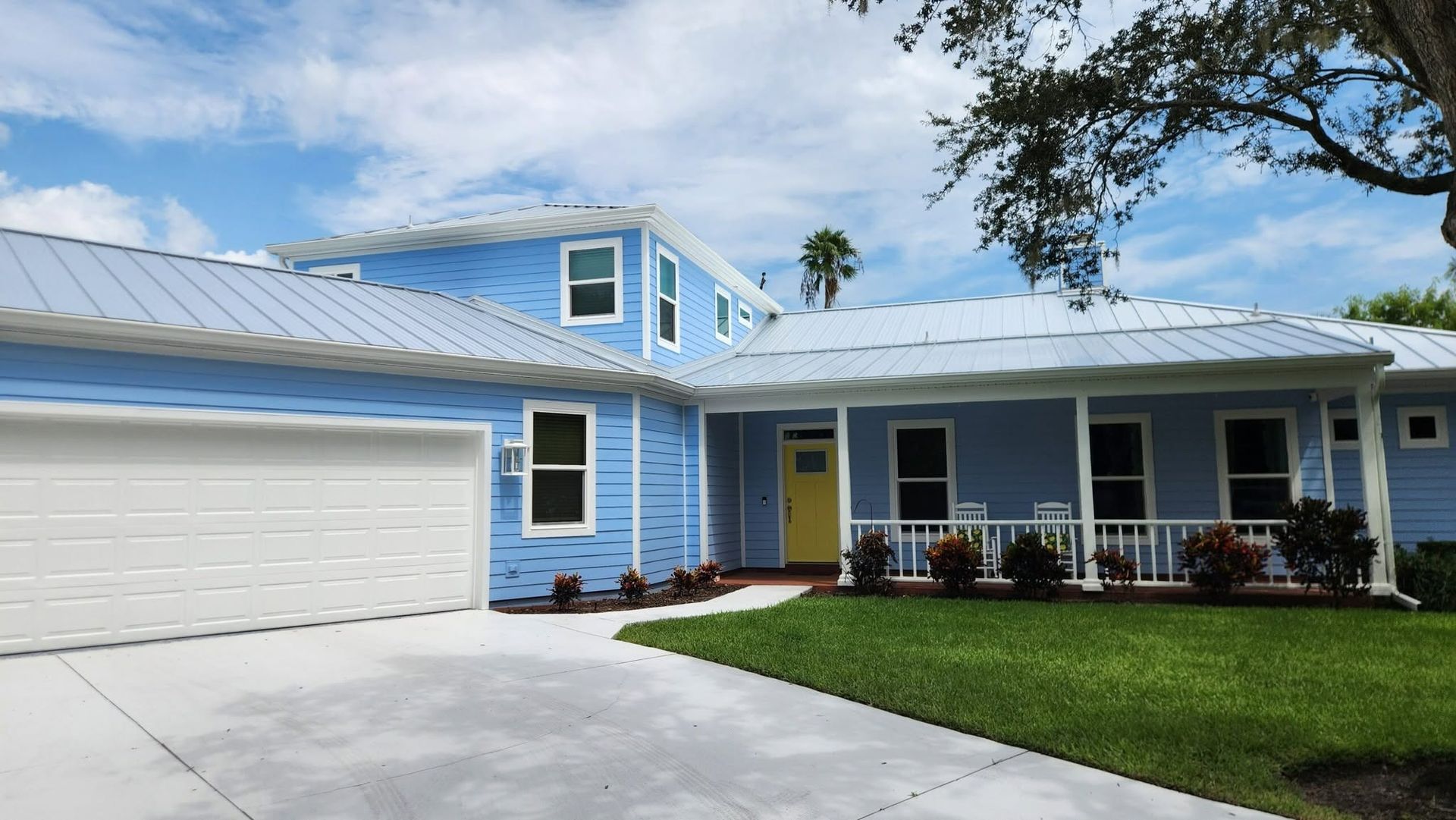 Light blue single-story house with white garage, yellow front door, and manicured lawn under a blue sky