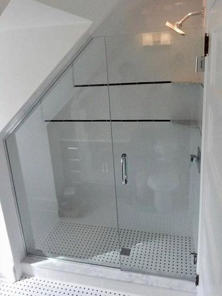 Glass shower enclosure in a white bathroom with a sloped ceiling and a patterned floor.