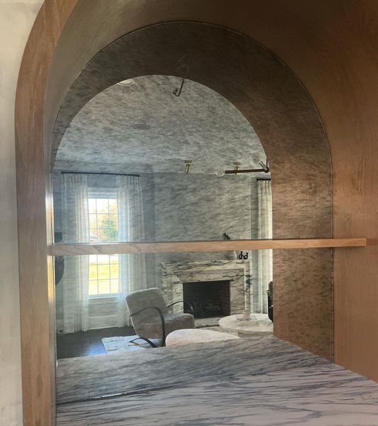 Archway revealing a living room with marble walls, a fireplace, and a window with curtains.