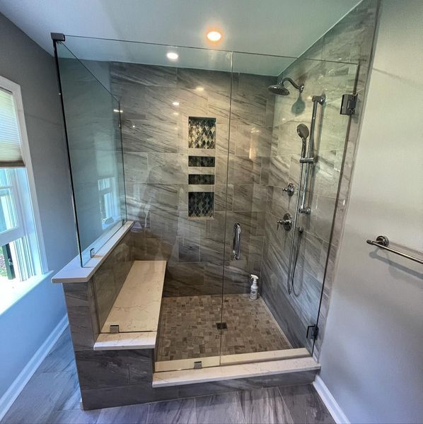 Modern gray and glass shower with bench, patterned tile, and recessed shelves.