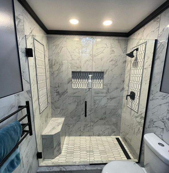 Modern bathroom with marble shower, black fixtures, and built-in bench.