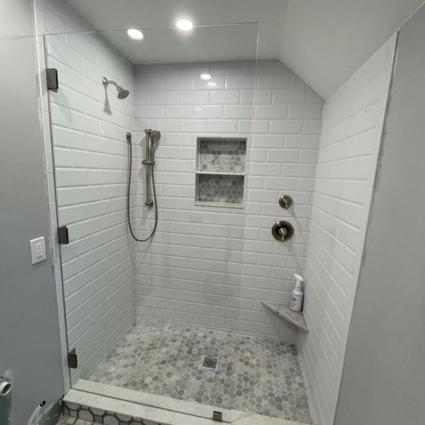 Modern bathroom shower with white subway tile walls, glass door, and pebble floor.