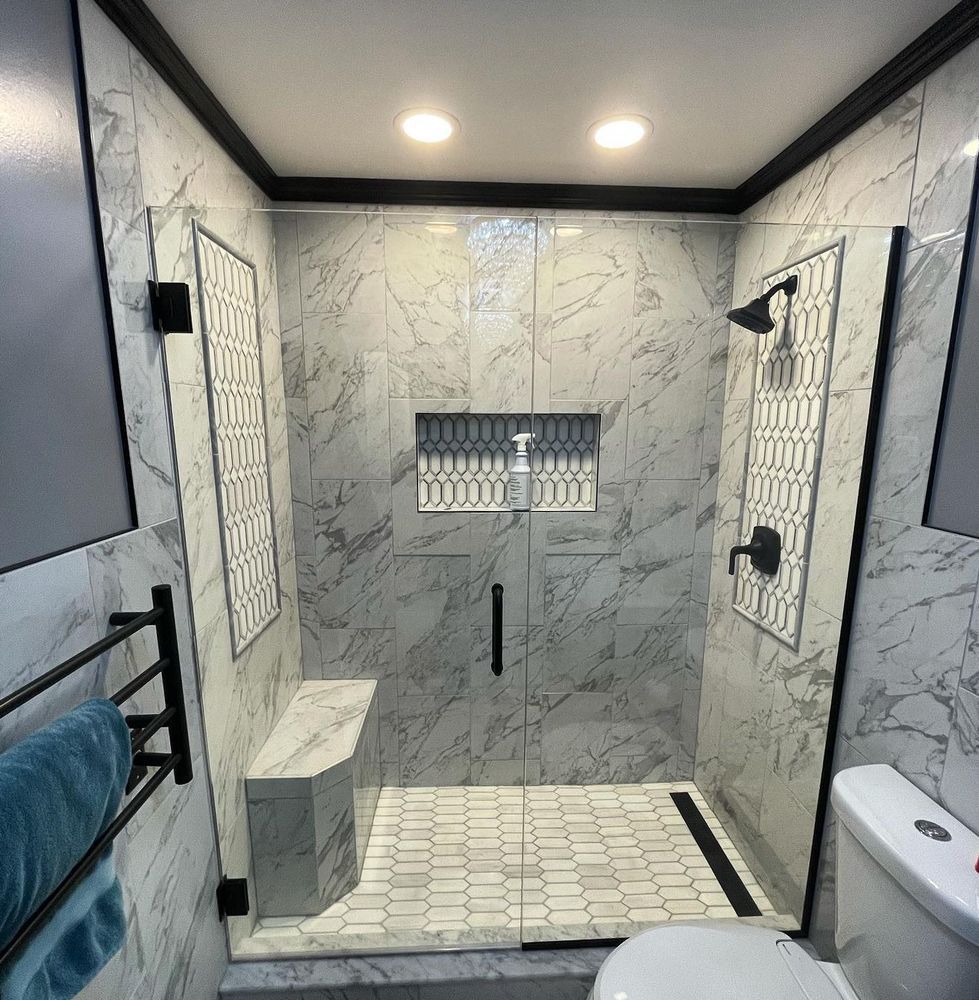Modern bathroom with a marble-tiled shower, glass door, bench, and black fixtures.