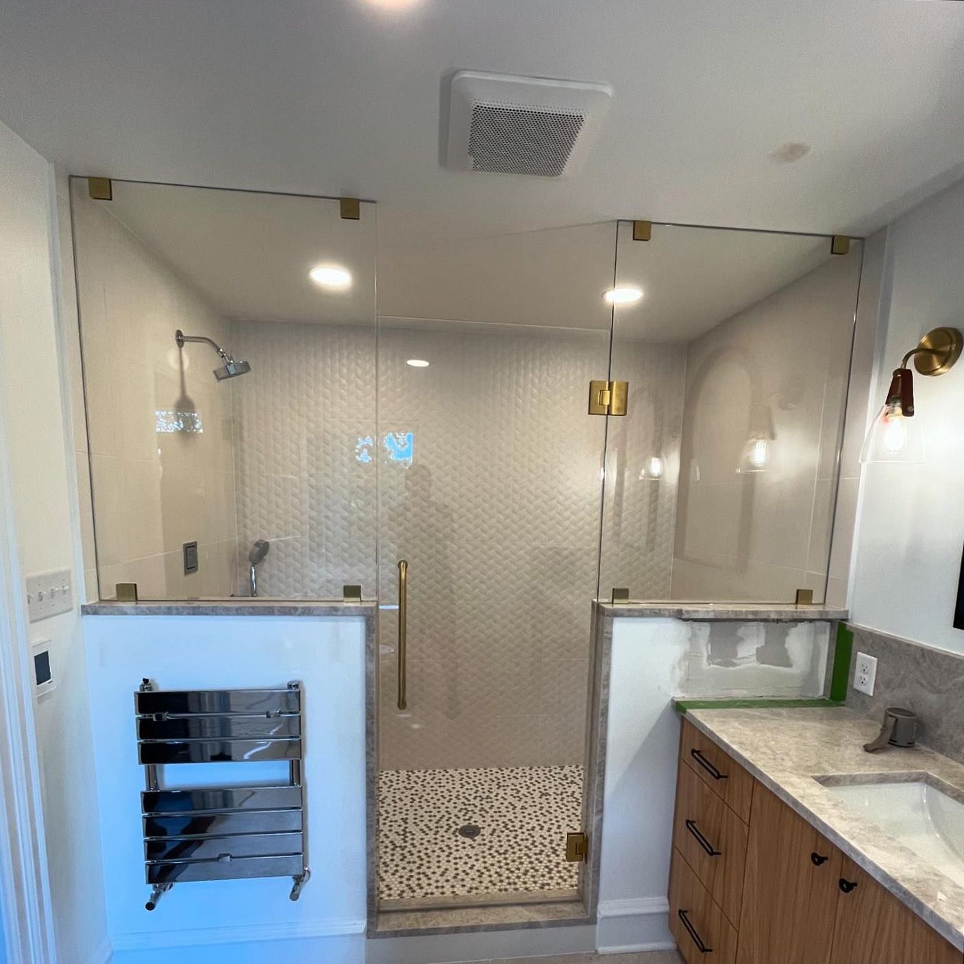 Bathroom with glass shower enclosure, gold fixtures, heated towel rack, wood vanity, and white tile.