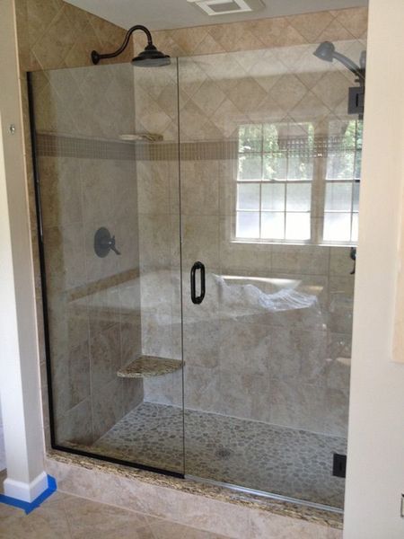 Glass shower enclosure with black fixtures and tan tile walls.