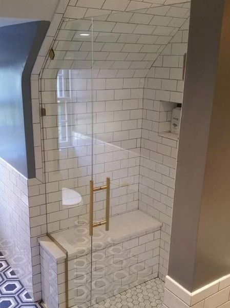 Glass-enclosed shower with white subway tiles, gold door handle, and built-in bench.