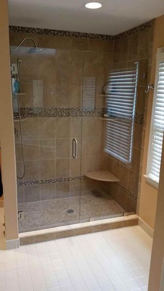 Shower with glass door, beige tile, a built-in bench, and a towel warmer.