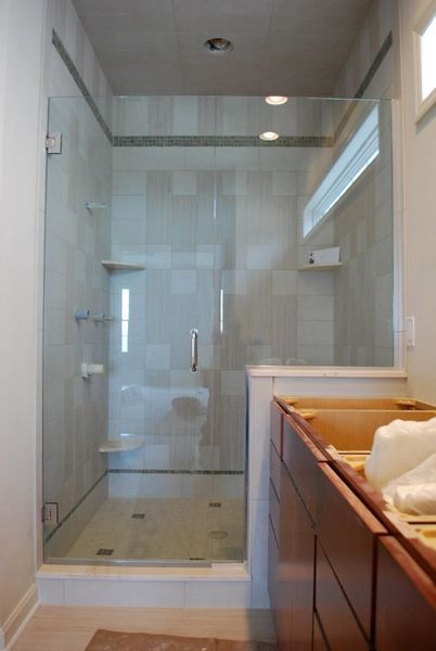 Glass shower enclosure with beige tiled walls, a wooden vanity, and recessed lighting.