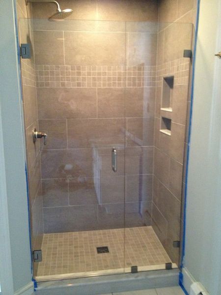 Glass shower stall with brown tile walls and mosaic tile floor.