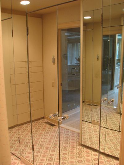 Mirrored closet with beige trim and pink patterned floor, open door reflecting the bathroom.