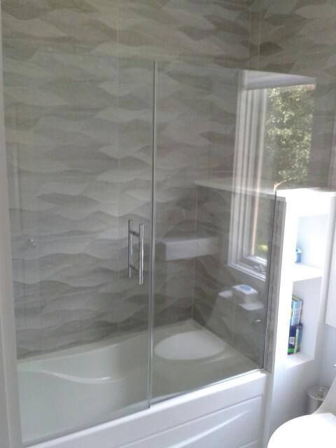 Bathroom with a tub, glass shower doors, and gray wave-patterned tile.