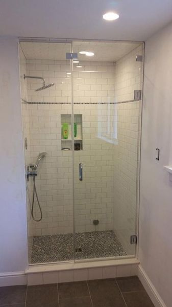 Glass shower enclosure with white tile walls and pebble floor.