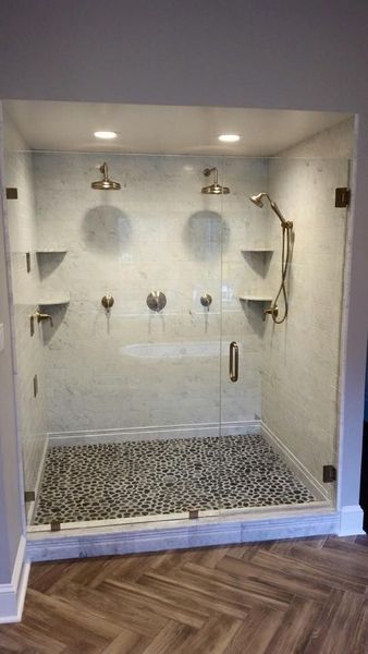 Large walk-in shower with pebble floor, glass walls, two shower heads, and built-in shelves.