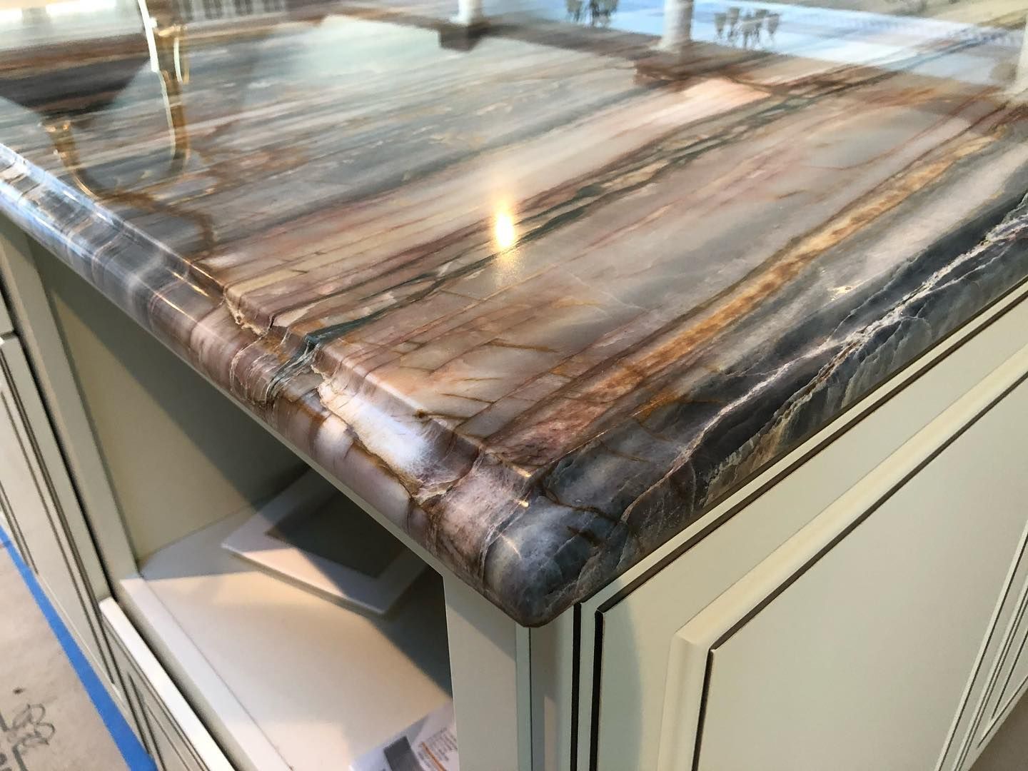 Brown and grey marbled countertop with rounded edge, atop cream cabinets.