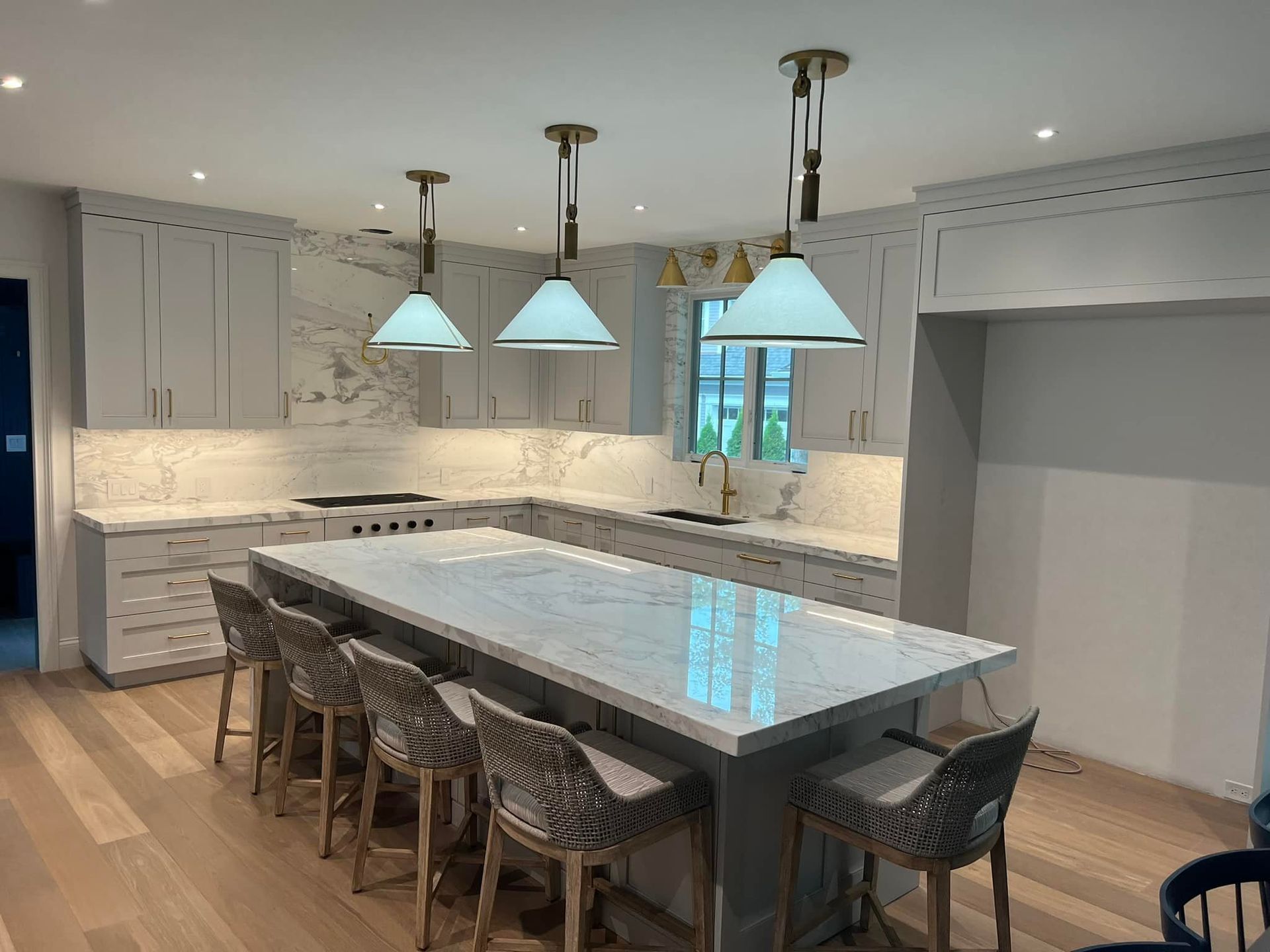 Modern kitchen with a gray island, cabinets, and marble countertops, with pendant lights and barstools.