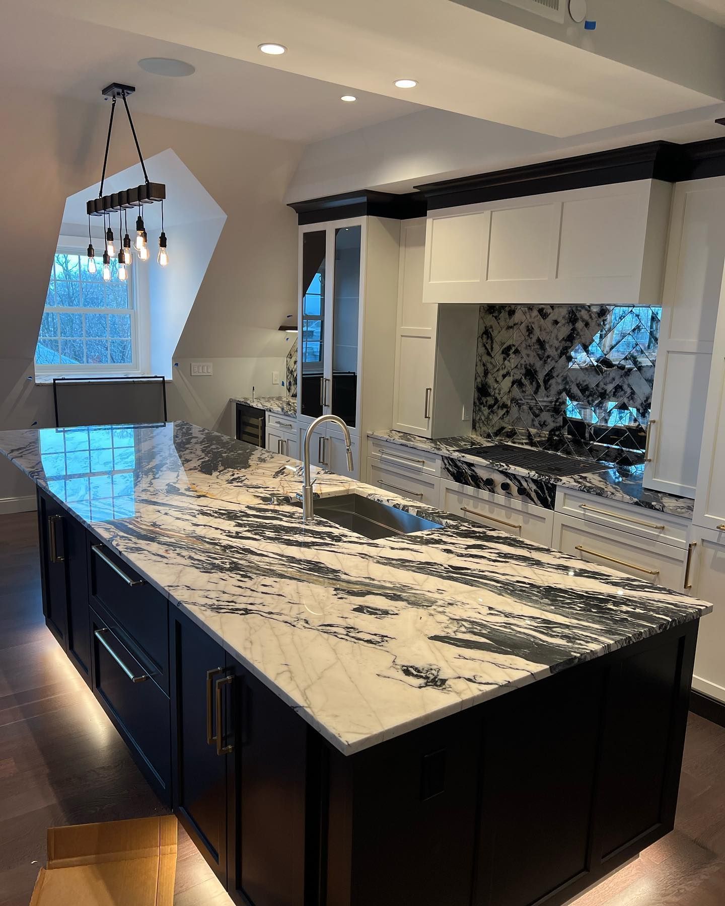 Kitchen with large black and white island, white cabinets, and a unique backsplash.