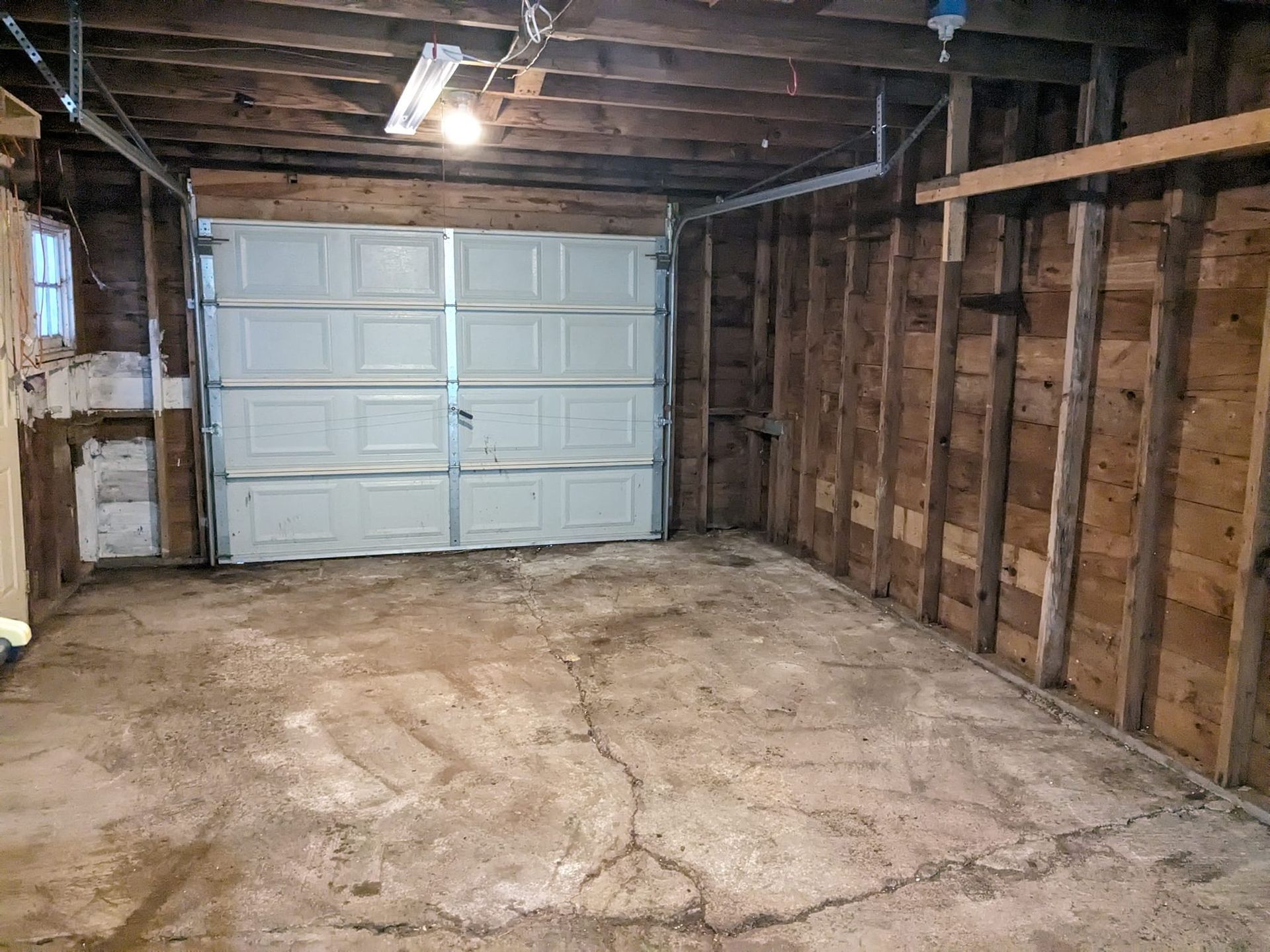An empty garage with a white garage door and wooden walls.