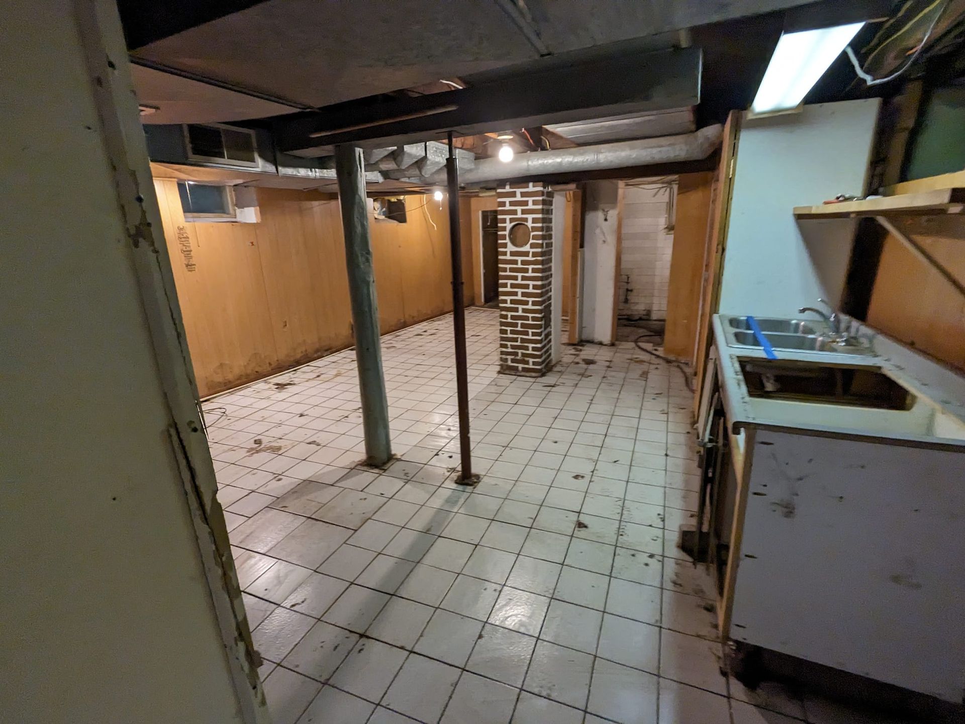 A kitchen in a basement with tile floors and a sink.