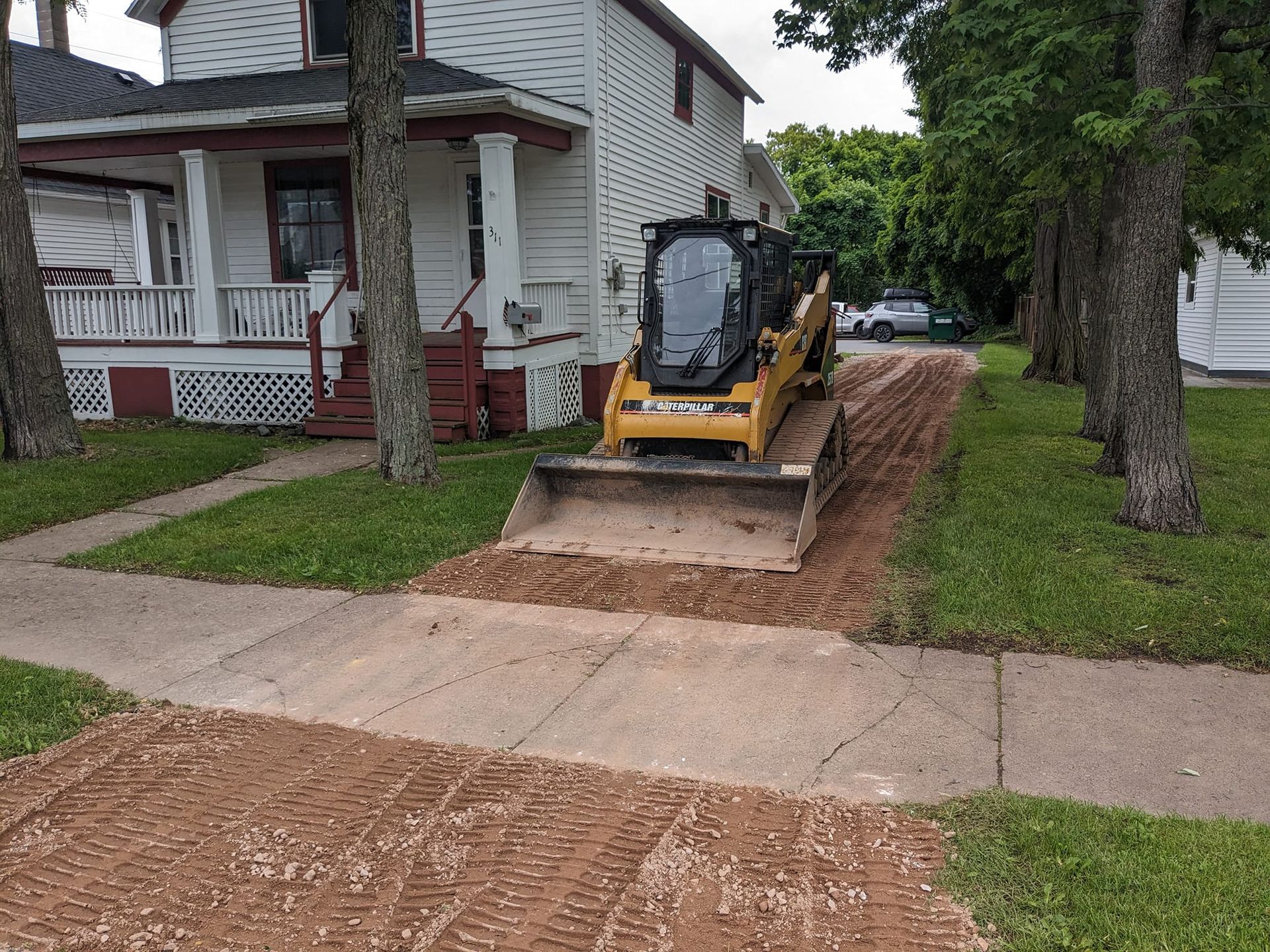 A bulldozer is moving dirt on a sidewalk in front of a house.