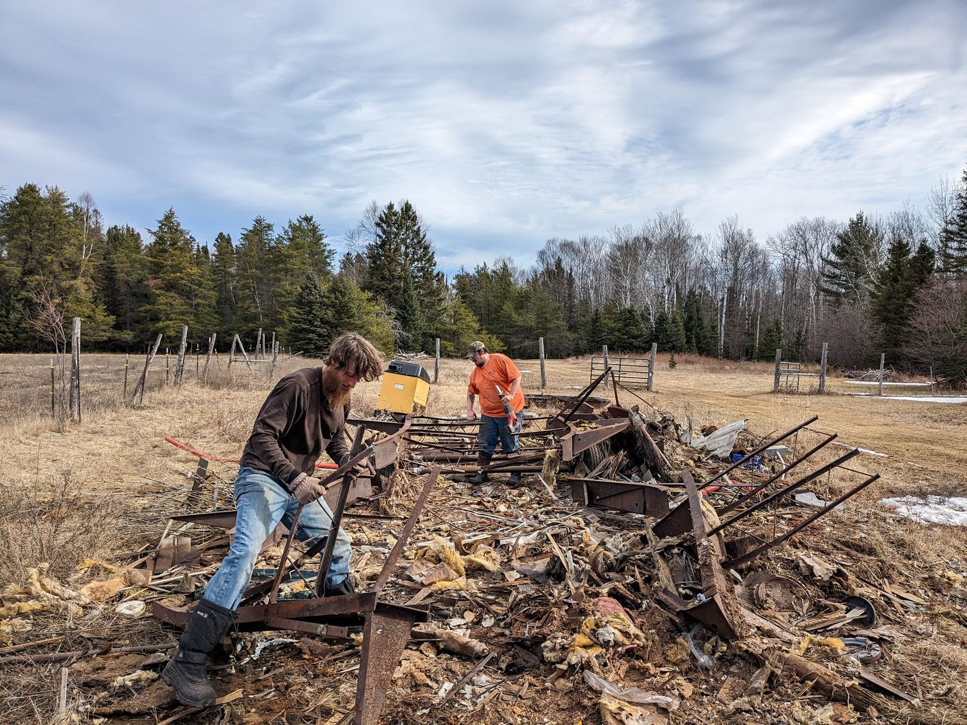 Two men are working on a pile of wood in a field.