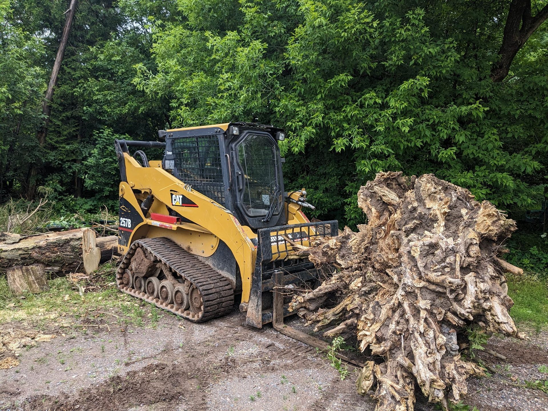 A bulldozer is moving a pile of logs in the dirt.