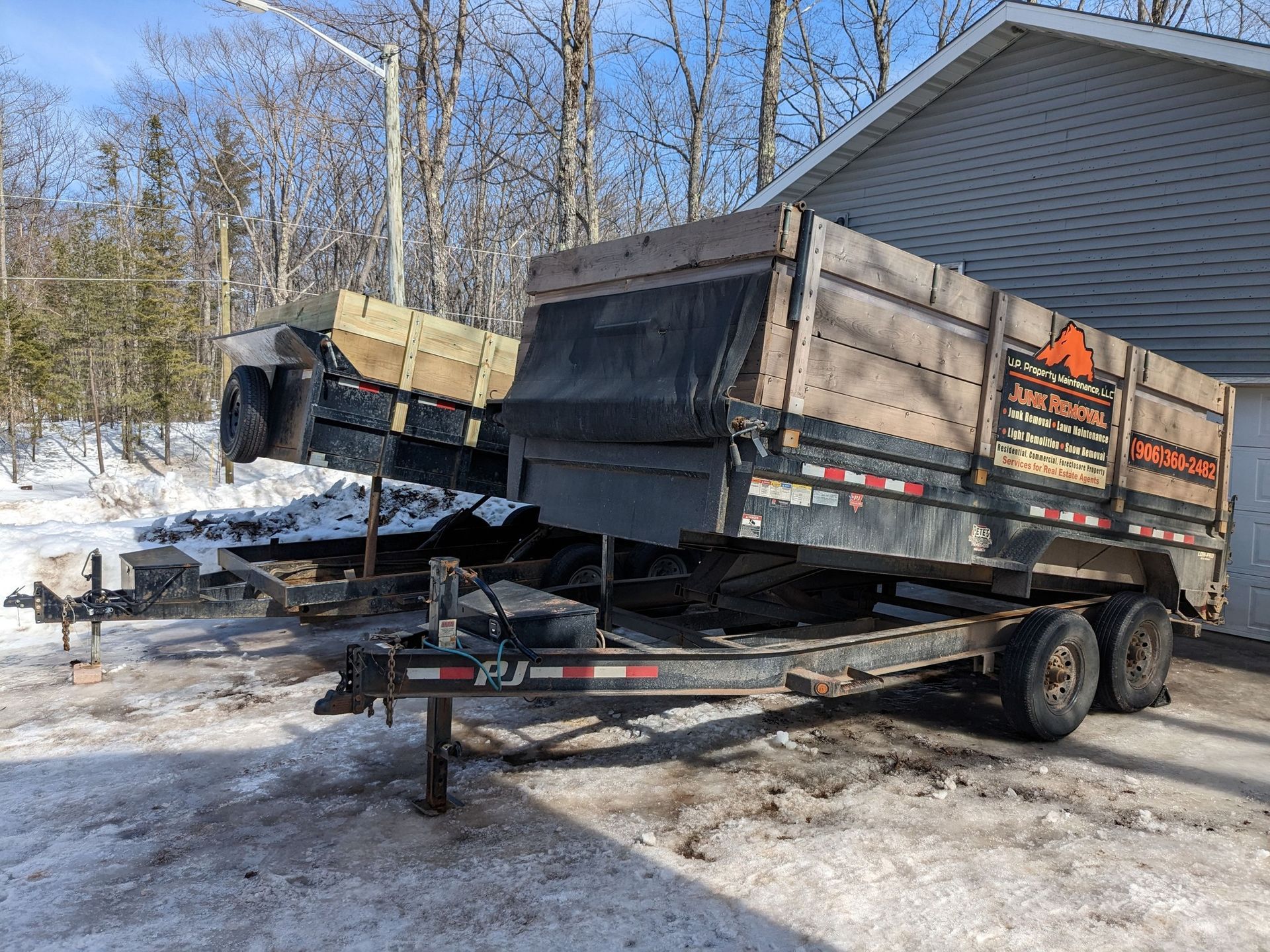 A dump trailer is parked in the snow in front of a house.