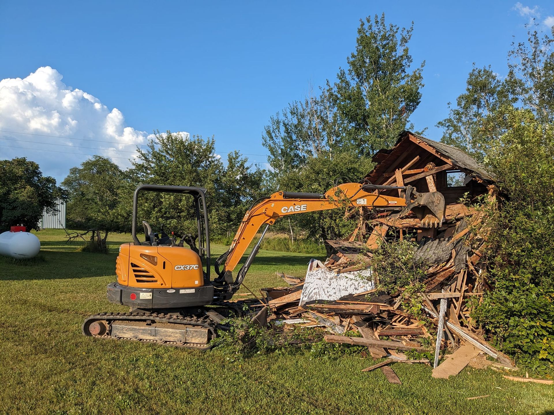 A small excavator is demolishing a building in a field.