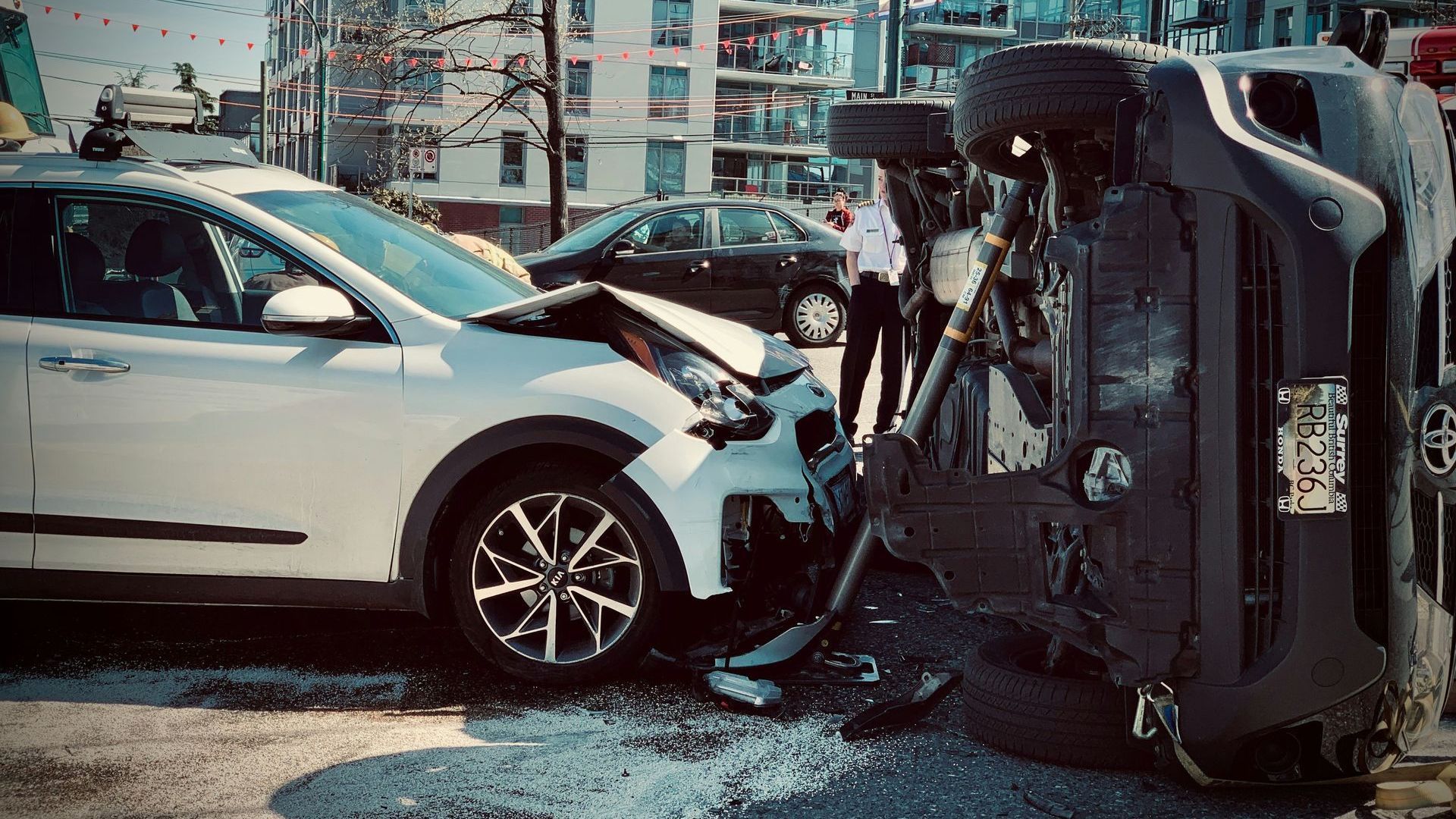 White SUV with heavy front-end damage after colliding with an overturned dark vehicle on a city street