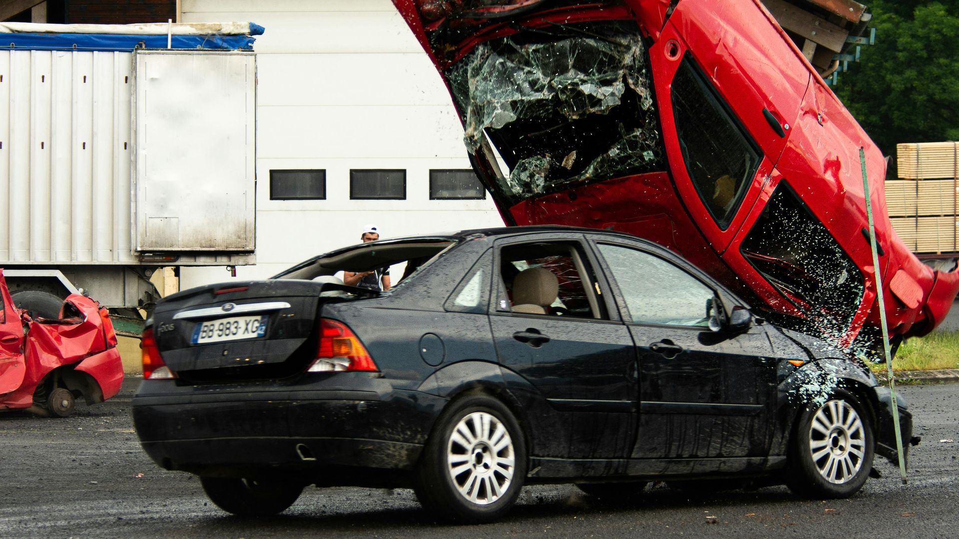 Black sedan hit by a red car in a collision, with the red car lifted onto the sedan’s hood.