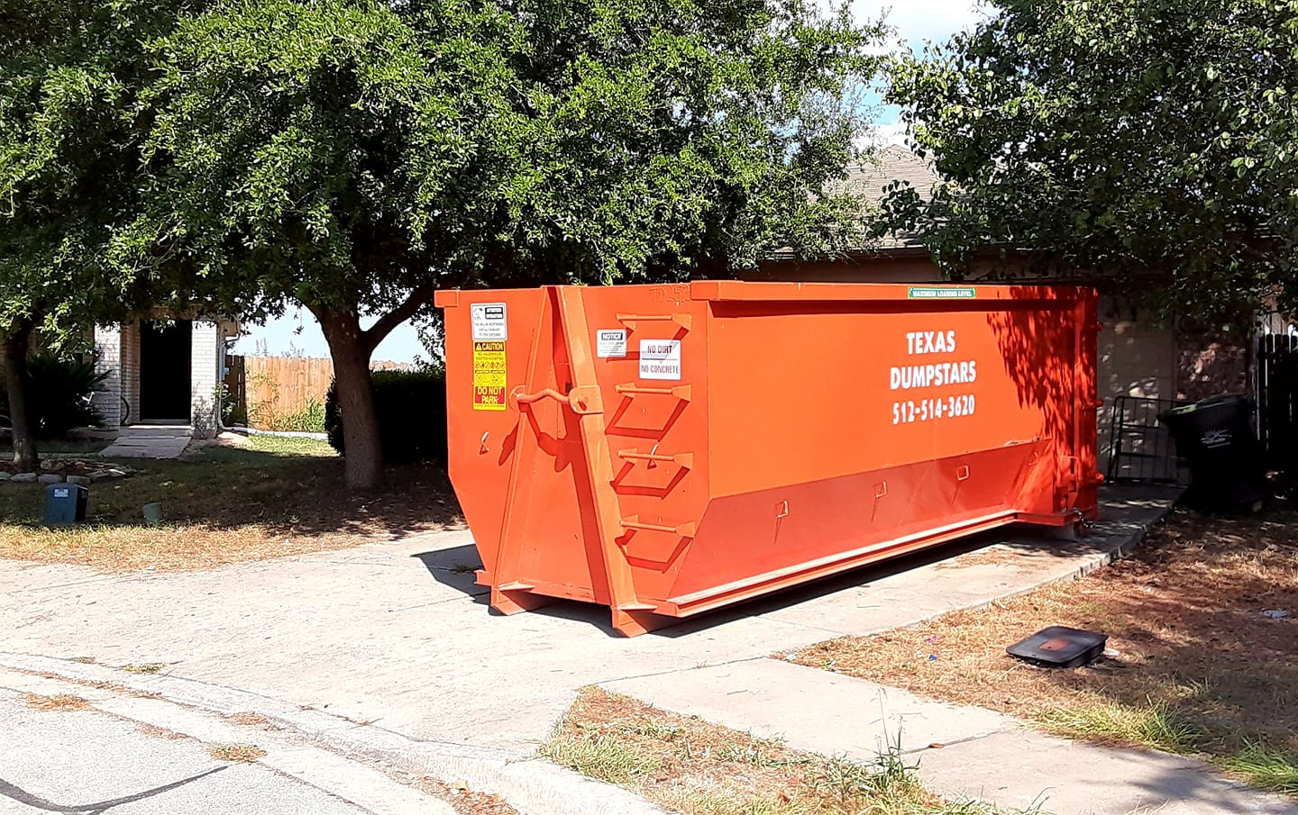 A large orange dumpster is parked in front of a house.