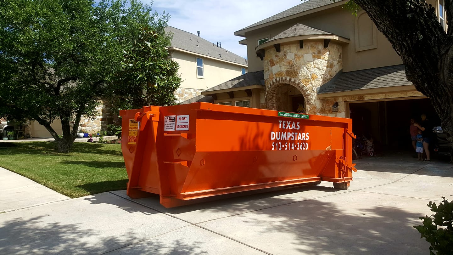 A large orange dumpster is parked in front of a house.
