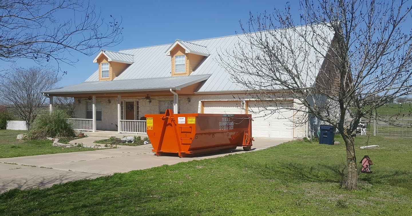 A large orange dumpster is parked in front of a house.