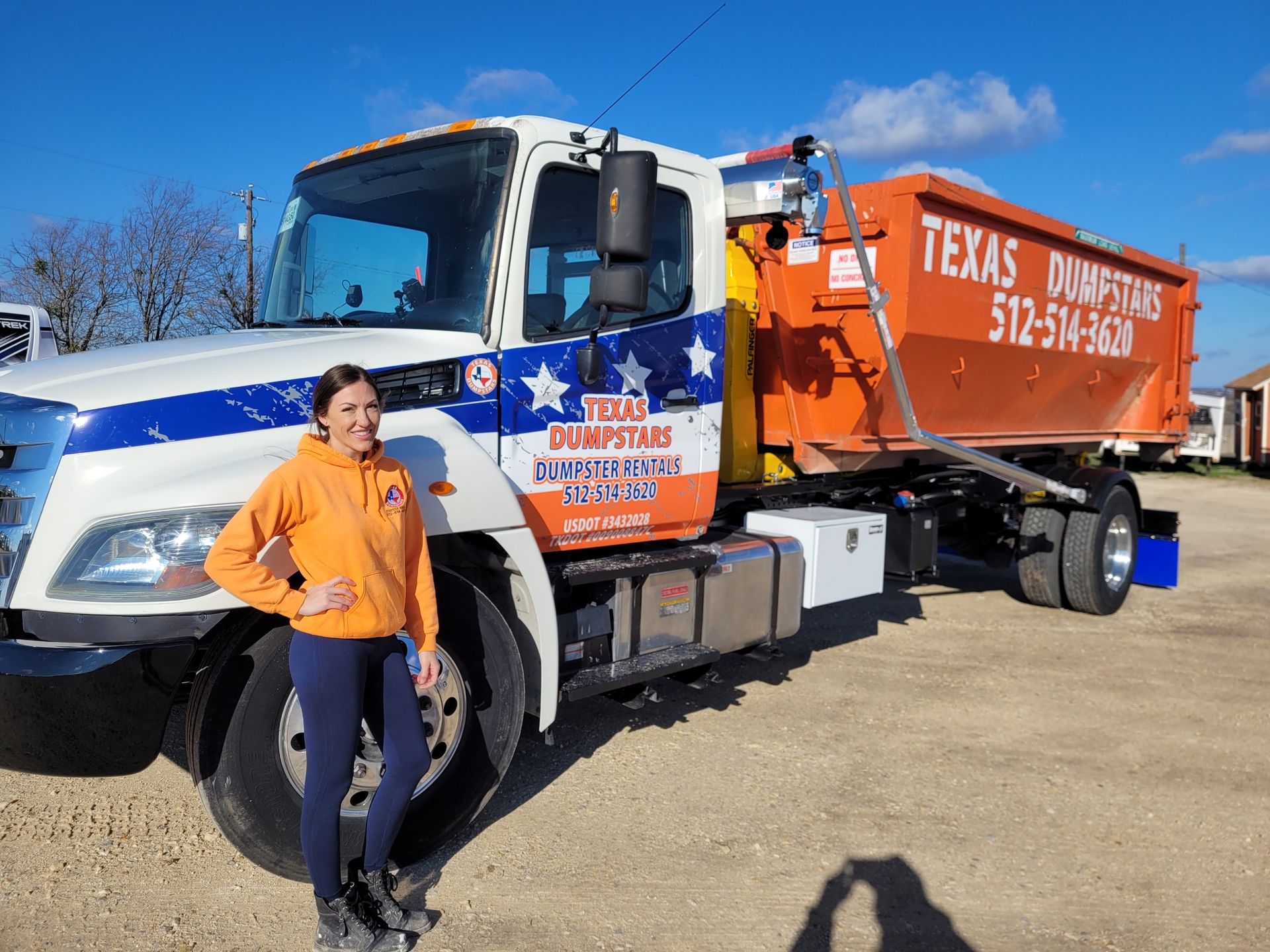 A woman is standing in front of a dumpster truck.