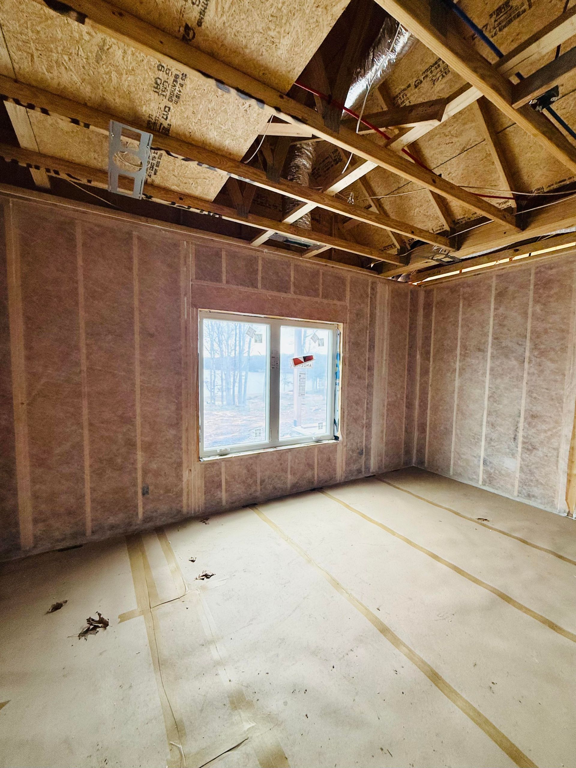 Unfinished room under construction with pink fiberglass insulation in the walls and visible wooden ceiling trusses.