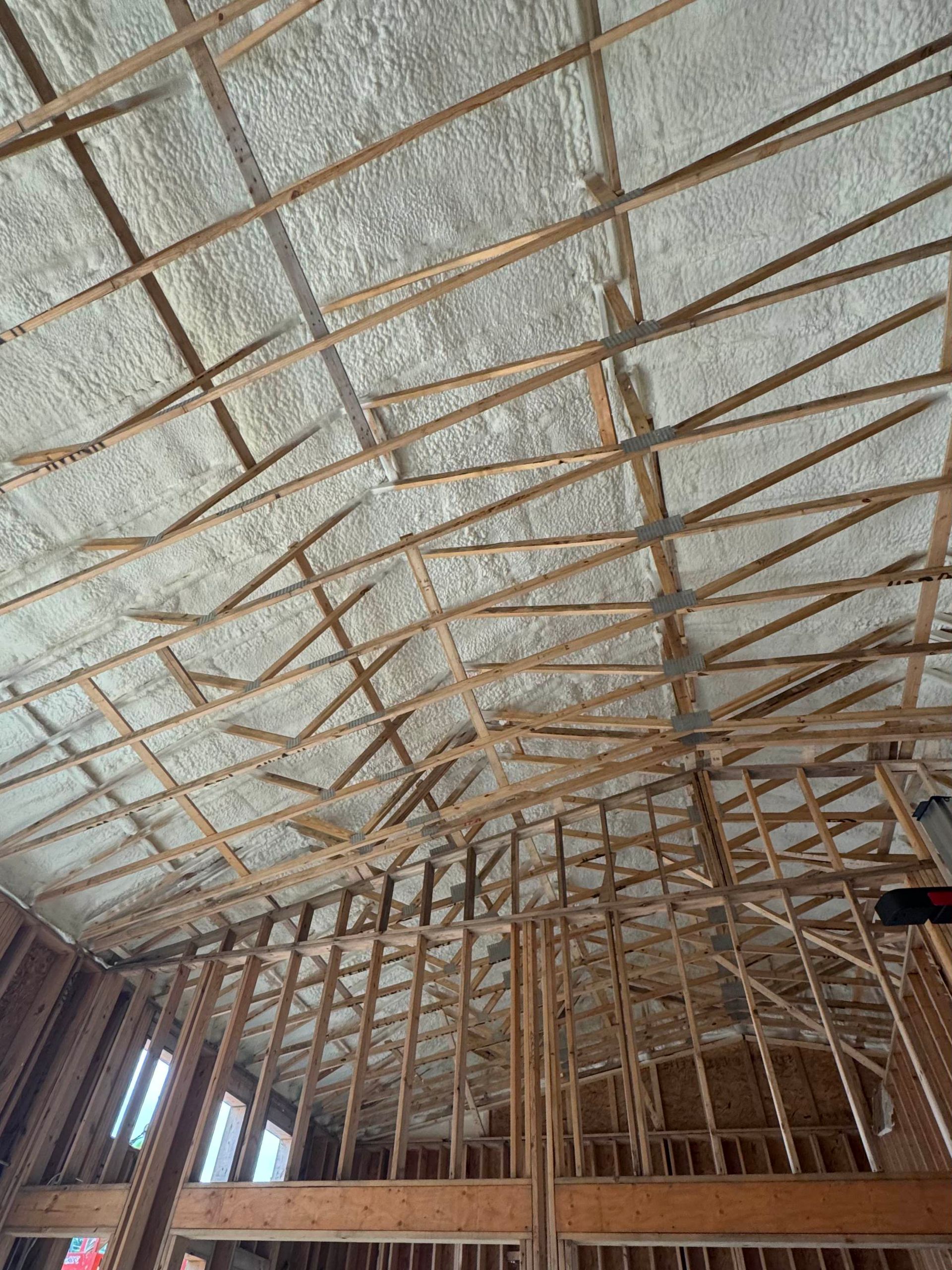 Interior view of a wooden attic frame with insulation foam applied to the underside of the roof.