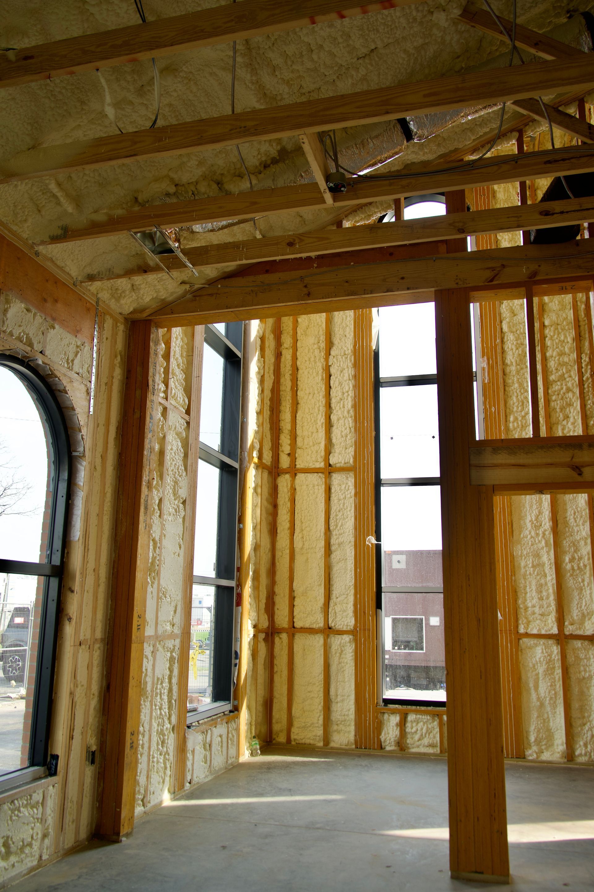 Interior view of a building under construction, featuring exposed wooden framing and walls insulated with spray foam.