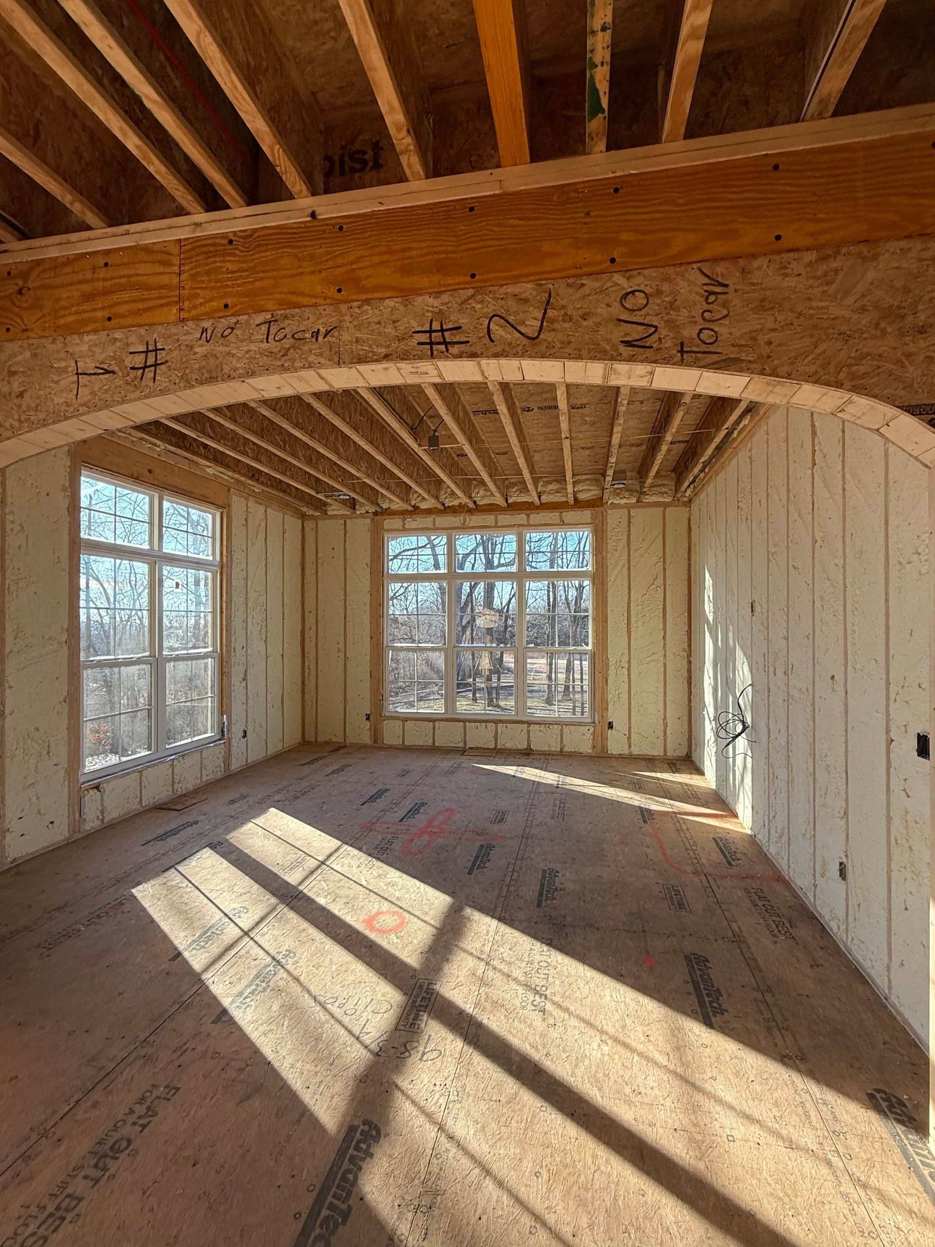 An interior view of a room under construction with exposed wooden framing, an arched header, and large windows.