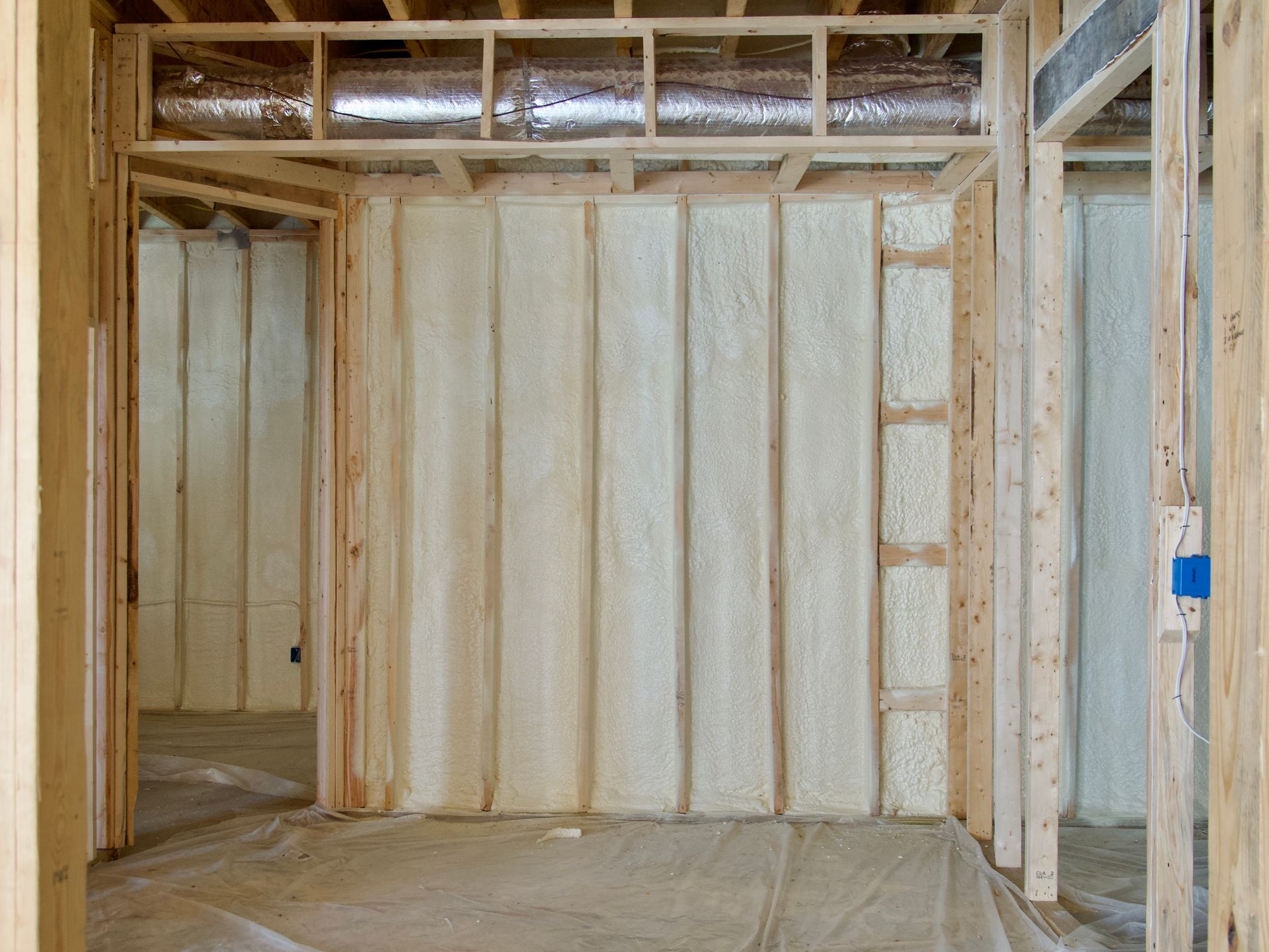 Interior view of a residential construction site featuring wood wall framing insulated with white spray foam.