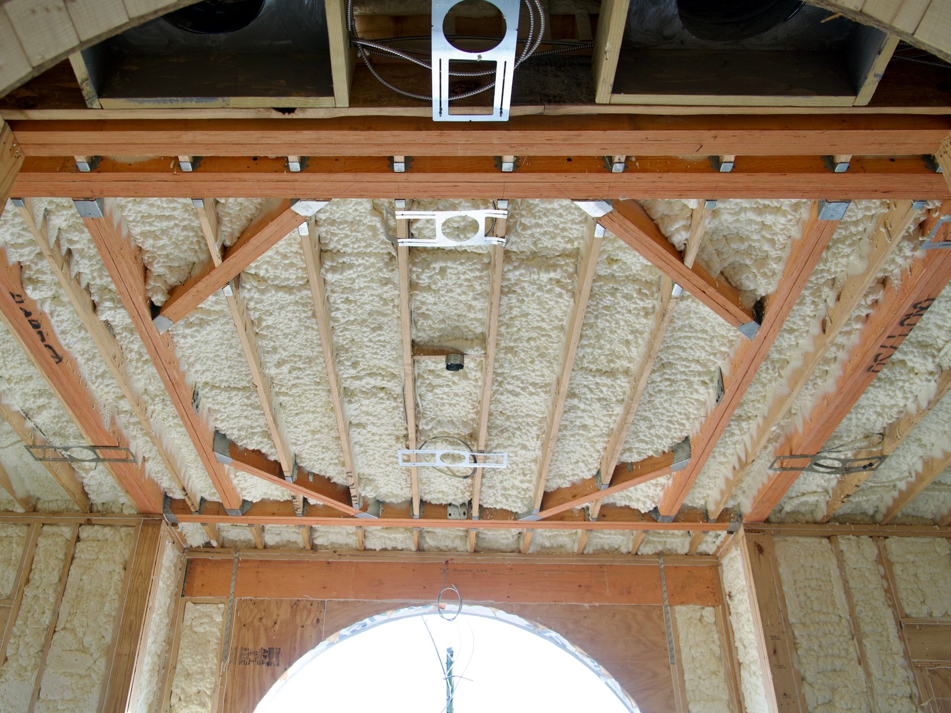 Unfinished ceiling and walls framed with wood and insulated with spray foam, featuring recessed lighting fixtures.