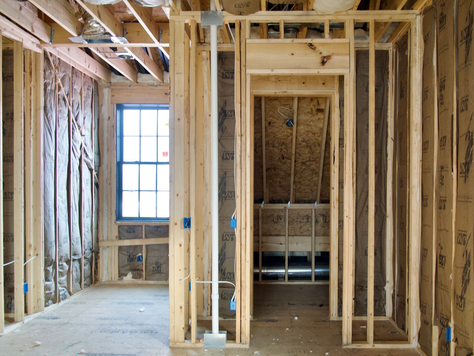 An interior room under construction featuring wooden wall studs, insulation, electrical wiring, and a framed doorway.