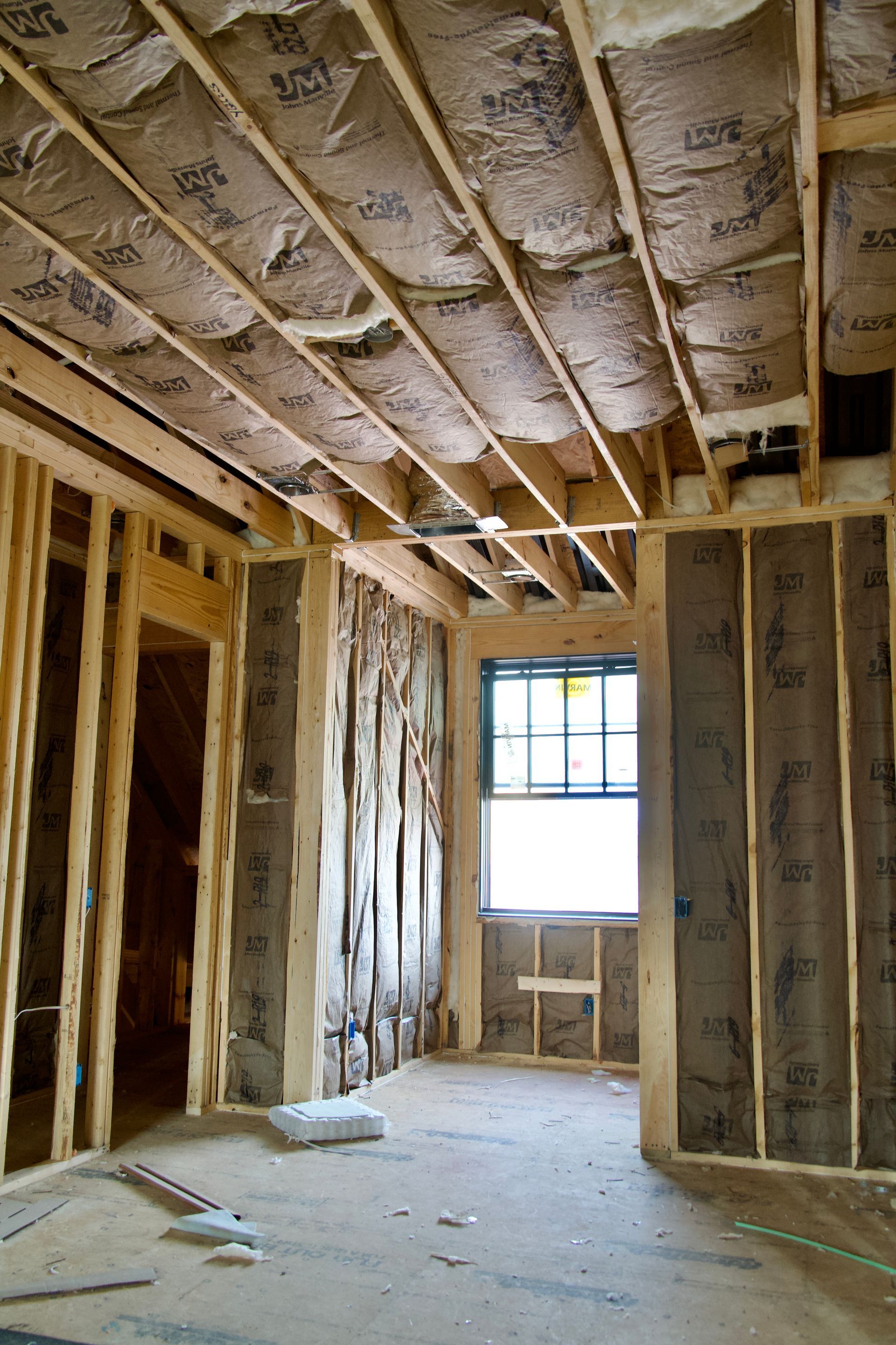 Interior of a room under construction with exposed wooden wall studs, insulation in the ceiling and walls, and a window.