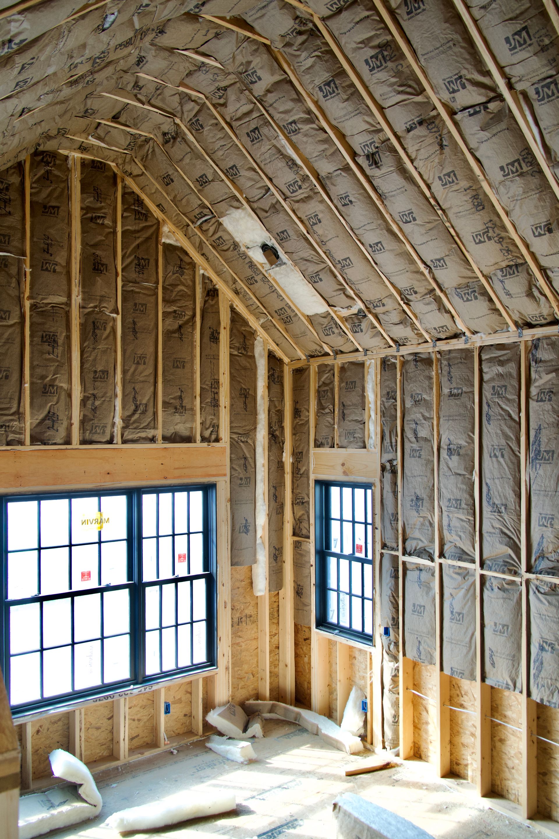 Interior of an unfinished room with exposed wooden framing and fiberglass insulation installed between the wall studs.