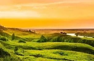 Rolling green hills under an orange sky, with a river in the distance.