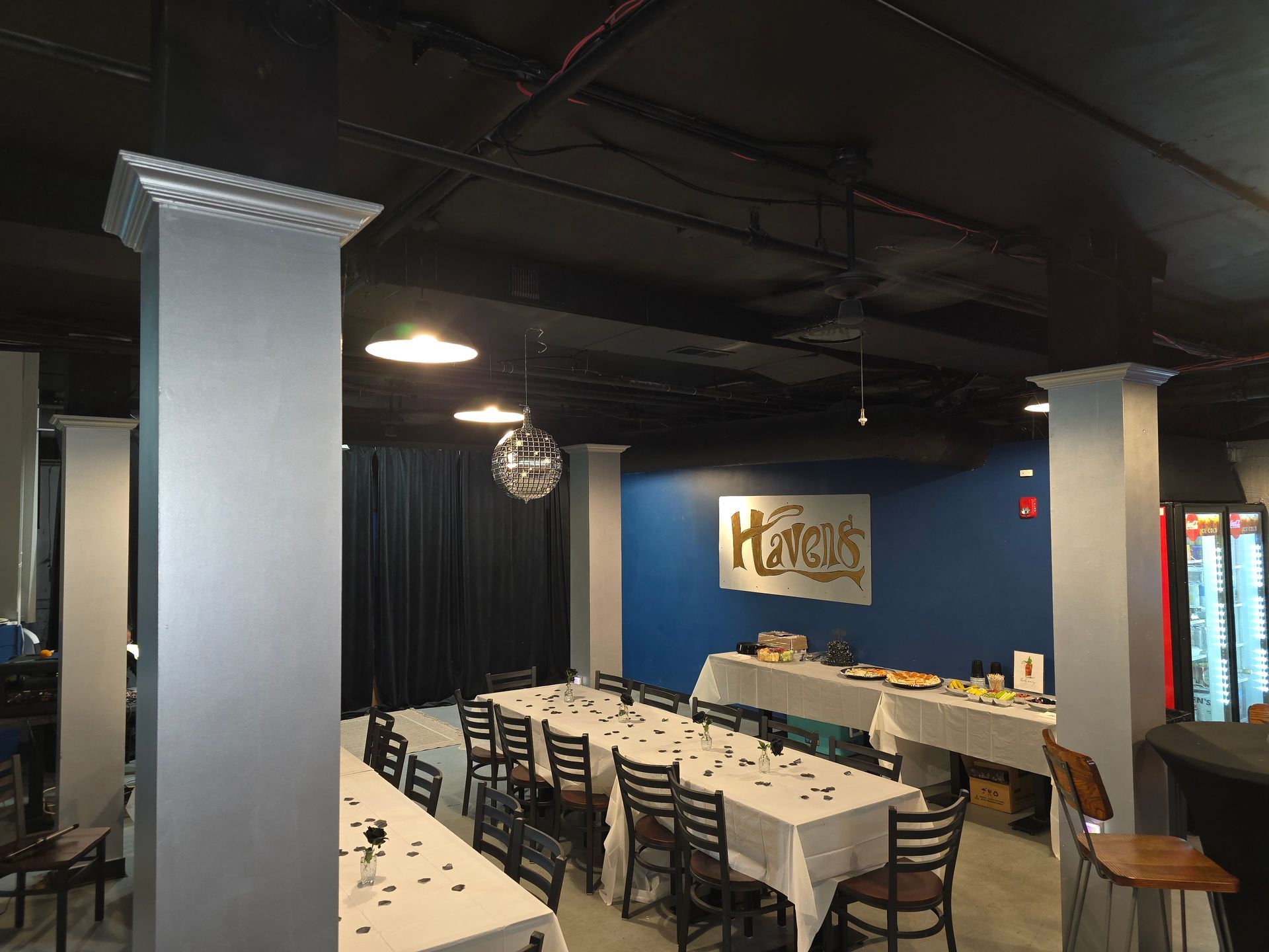 Interior view of a party venue with tables set for guests. Disco ball hangs over a black curtain.