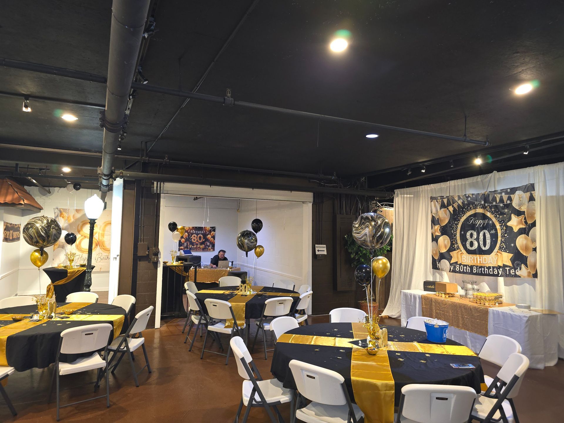 Party room decorated in black and gold for a 60th birthday celebration with tables, chairs, and a banner.