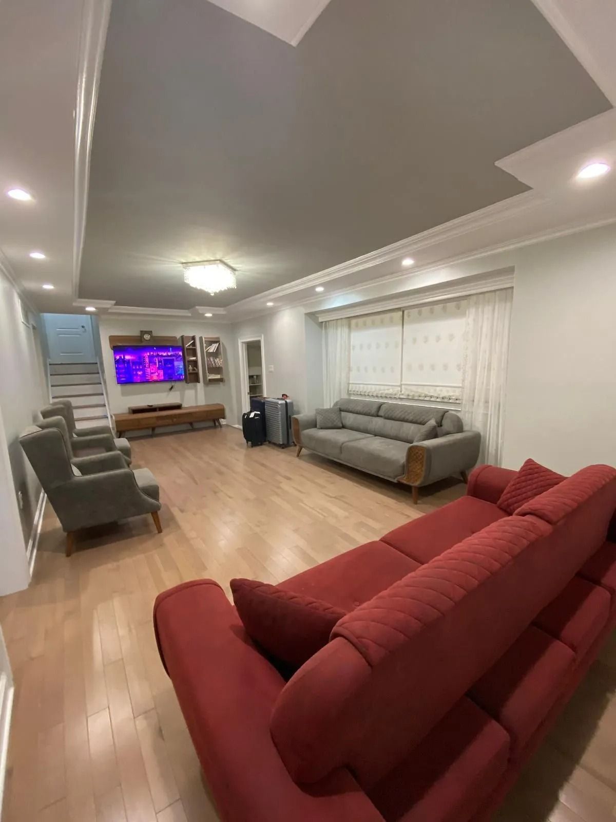 Living room with red and gray couches, wooden floors, and a TV on the wall.
