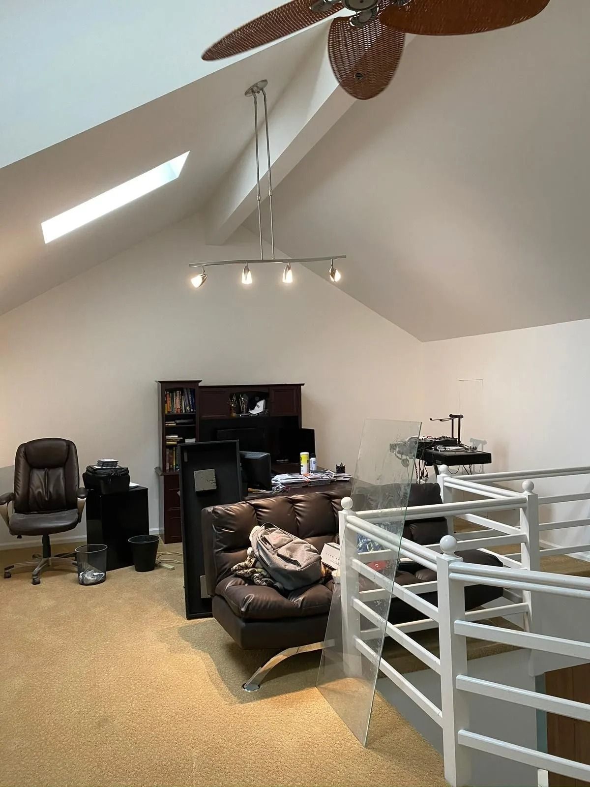 Loft interior with angled ceiling, desk, couch, and railing. Brown and white color scheme.