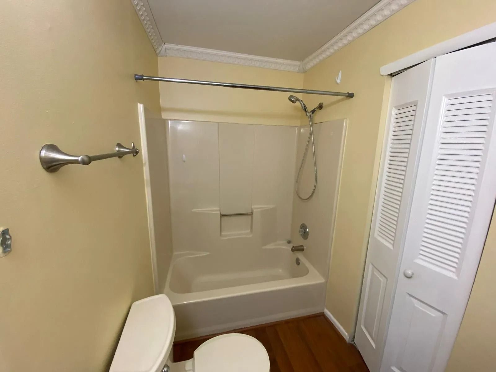 Bathroom with a white tub and toilet, showerhead, and a towel rack on the wall.
