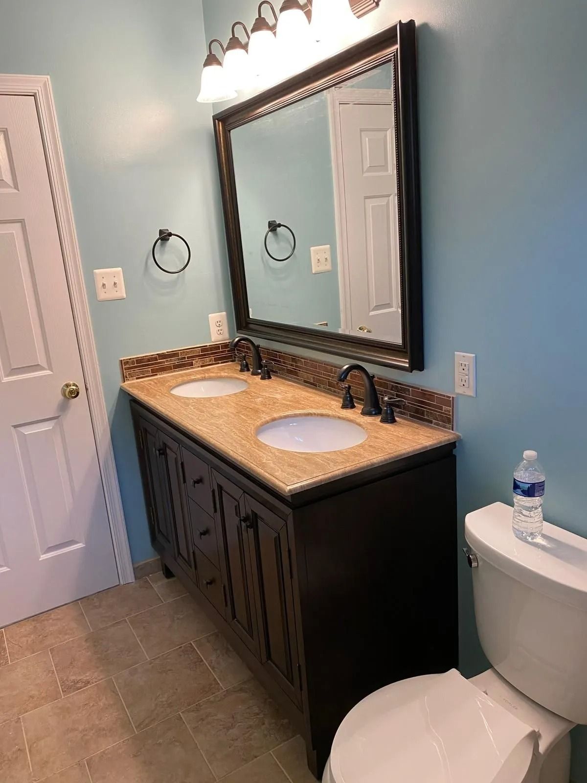 Bathroom with double vanity, beige countertop, dark cabinets, framed mirror, and blue walls.