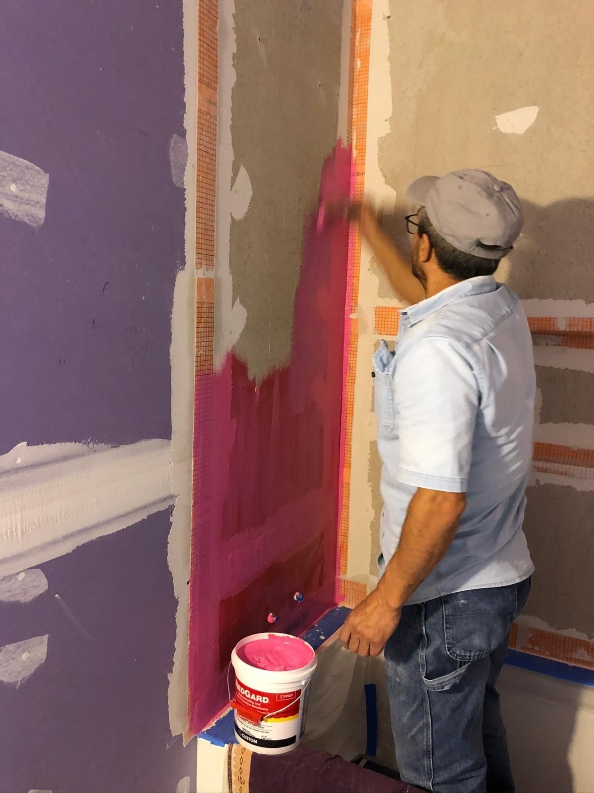 A person applies pink joint compound to a wall's corner.